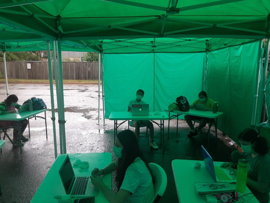 high school class in outdoor classroom tents during rain